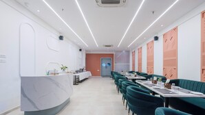 A modern dining area with a marble reception desk, teal upholstered booths, and a long table with white tablecloths. - Treebo Premium Aasma Courtyard (Kujang)