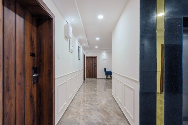 A hallway with a wooden door labeled "304", a blue chair, and a marble floor. - Treebo Premium Aasma Courtyard (Kujang)