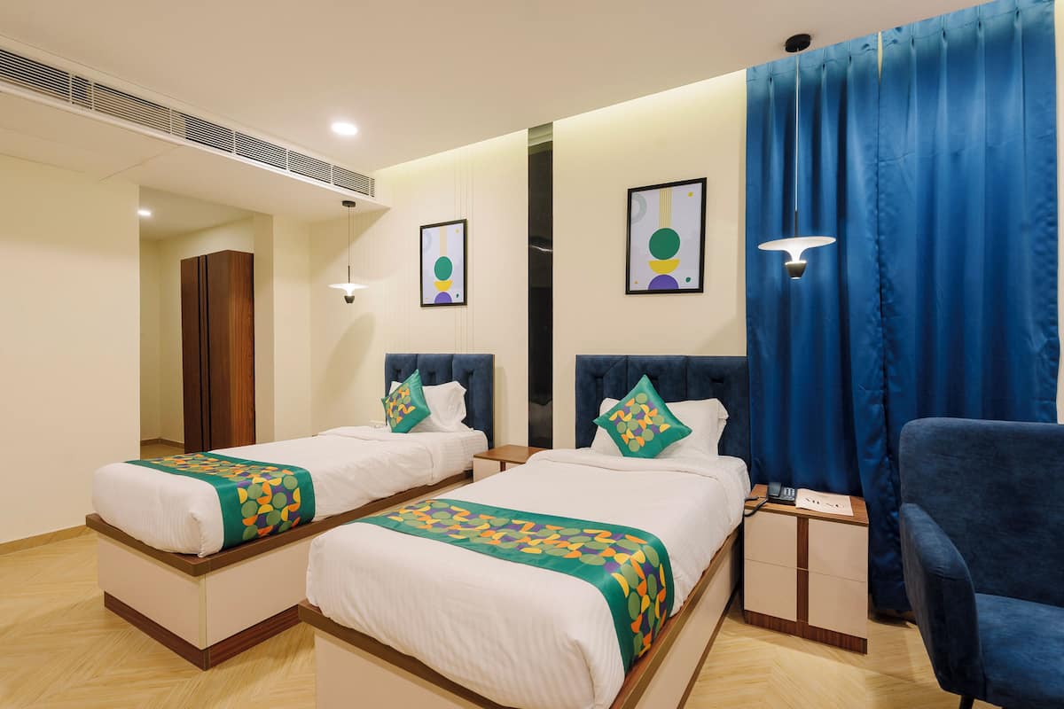A hotel room with two beds, a desk, a chair, and a large window with curtains.