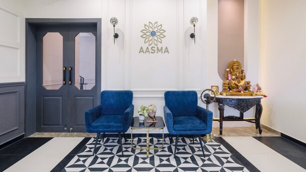 A reception area with a black and white geometric patterned floor, two blue armchairs, a small table with a globe and flowers, a decorative table with a golden statue, and a door with a logo on the wall. - Treebo Premium Aasma Courtyard (Kujang)