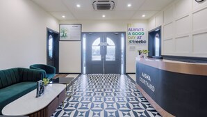 A reception area with a geometric patterned floor, a reception desk labeled "AASMA COURTYARD," a green sofa, and a framed tree illustration on the wall. - Treebo Premium Aasma Courtyard (Kujang)