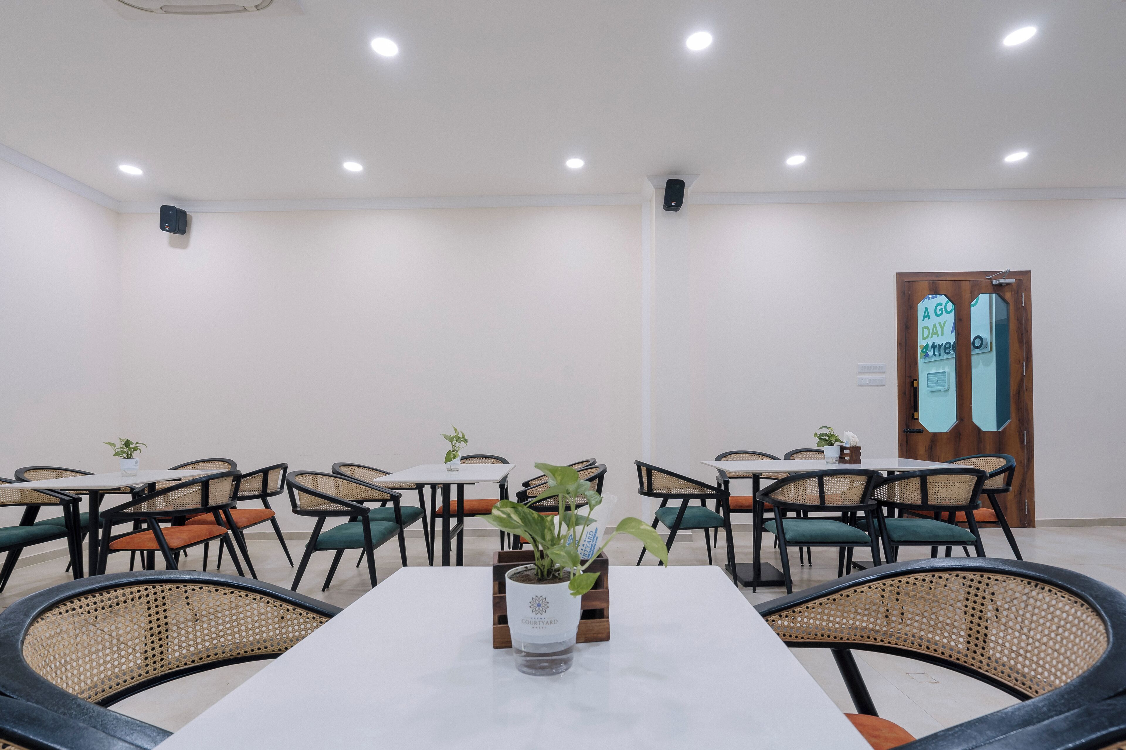 Un salón de conferencias con una mesa blanca, sillas negras y una planta en maceta.