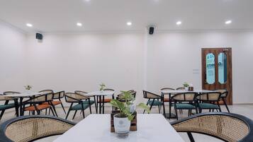Un salón de conferencias con una mesa blanca, sillas negras y una planta en maceta.