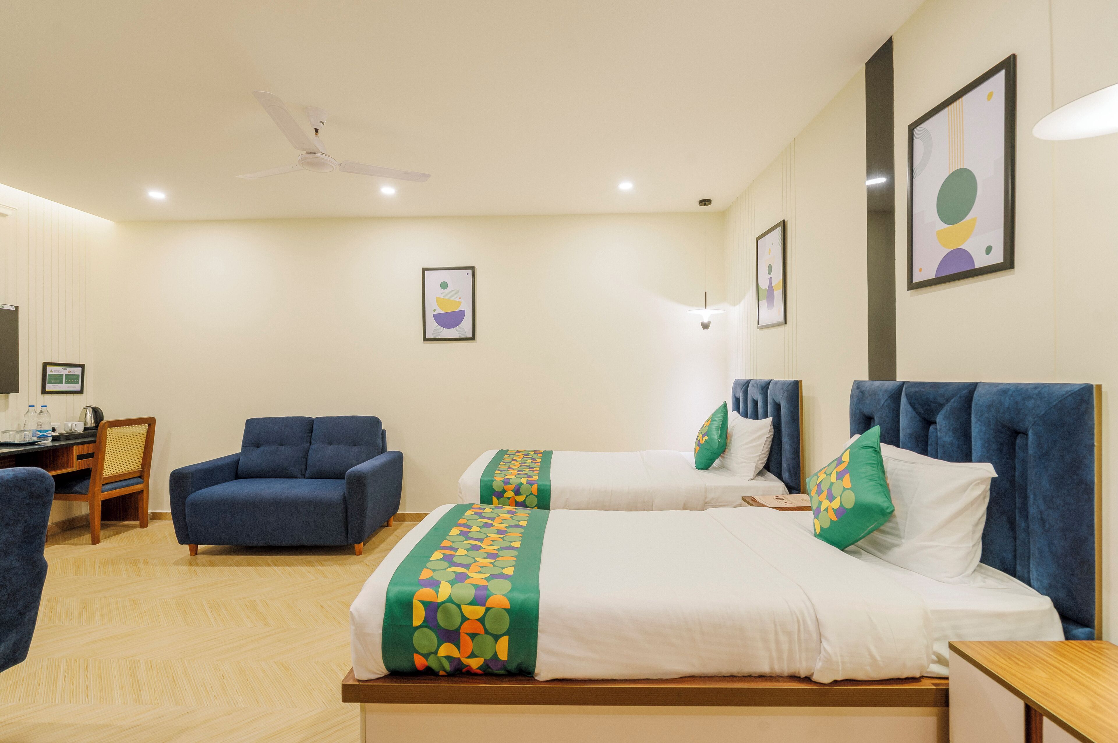 A hotel room with two beds, a desk, a chair, and a ceiling fan.