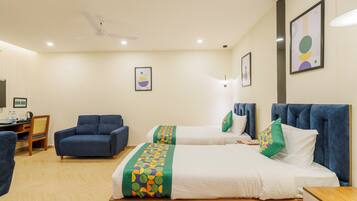 A hotel room with two beds, a desk, a chair, and a ceiling fan.