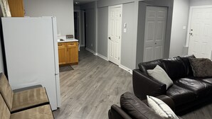 A modern living room with a leather sofa, a white refrigerator, wooden cabinets, and grey walls.