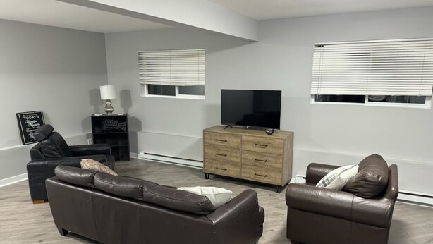 A modern living room with a sectional sofa, a smaller sofa, a TV on a wooden cabinet, and a side table with a lamp.