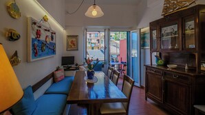 Zona pranzo con tavolo in legno, sedute imbottite blu, televisore e oggetti decorativi alle pareti.