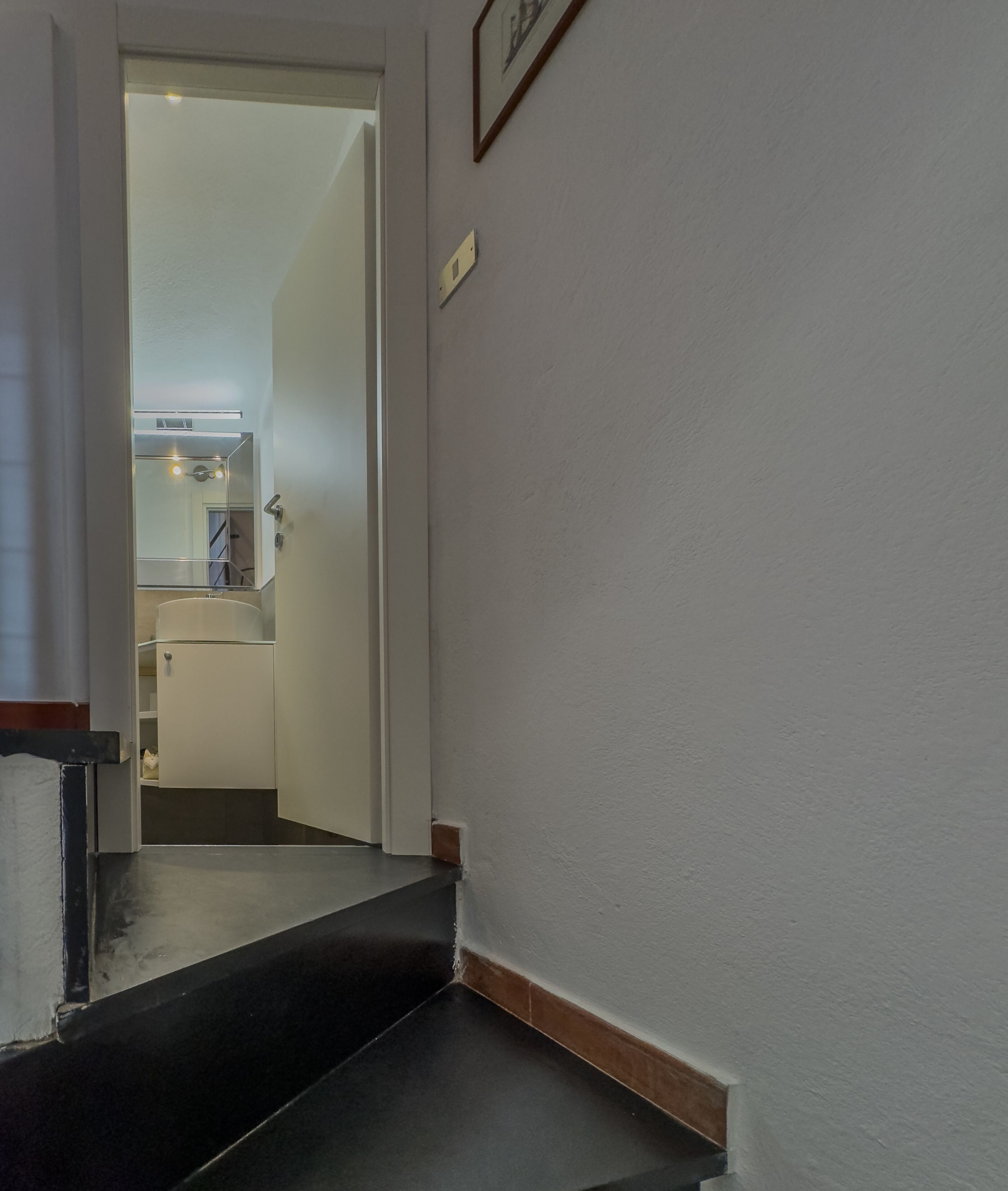 Un pasillo con alfombra negra que conduce a una habitación con puerta blanca.