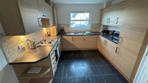 A modern kitchen with a gas stove, a sink, and wooden cabinets. - Kingfisher Apartment (Fife)