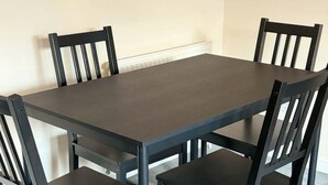 Una mesa rectangular de comedor con cuatro sillas, todo en colores oscuros.