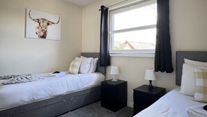 Un dormitorio con cama, dos mesitas de noche, una ventana con cortinas y una obra de arte en la pared.