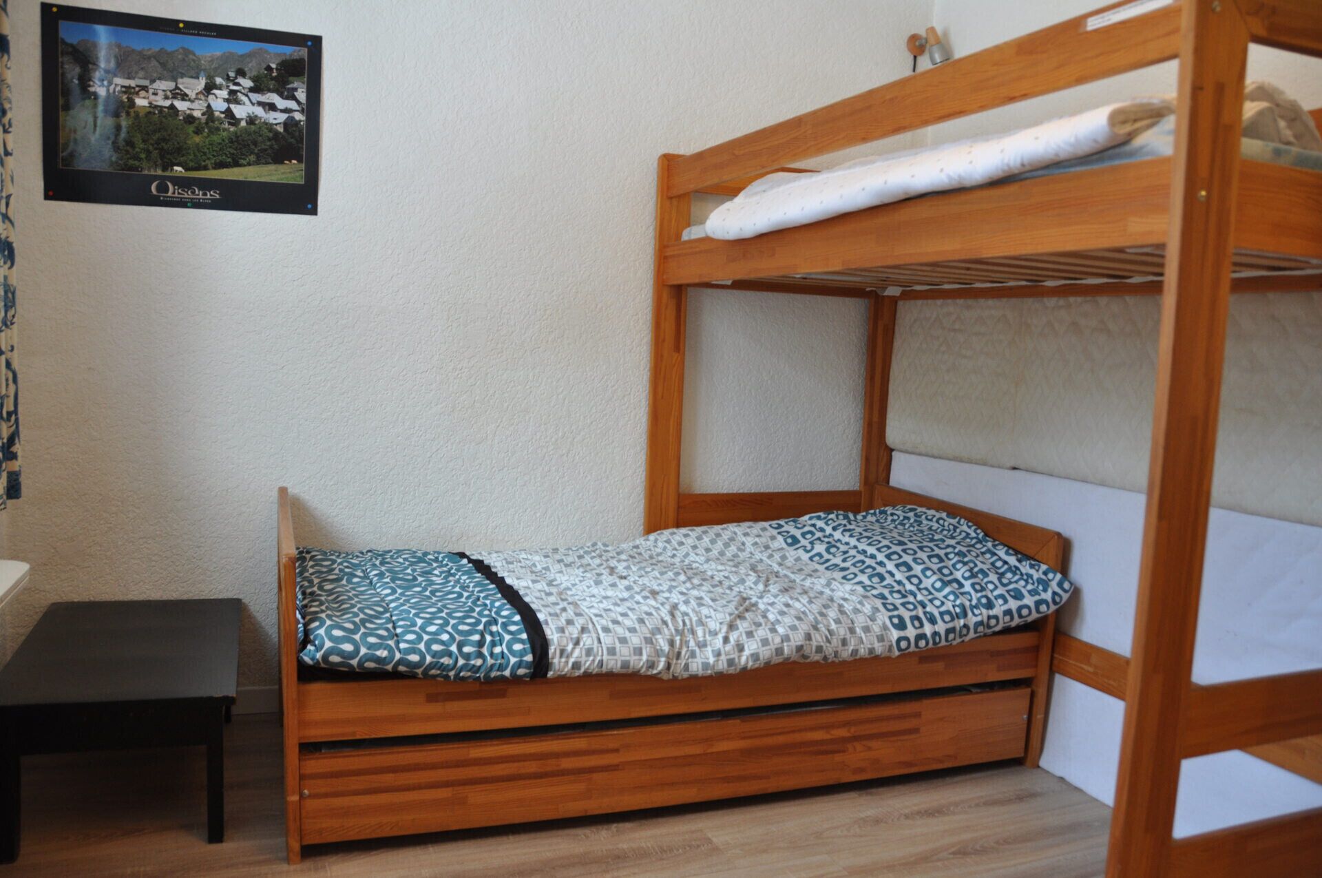 A bunk bed with a patterned bedspread, a small wooden table, and a framed picture on the wall.