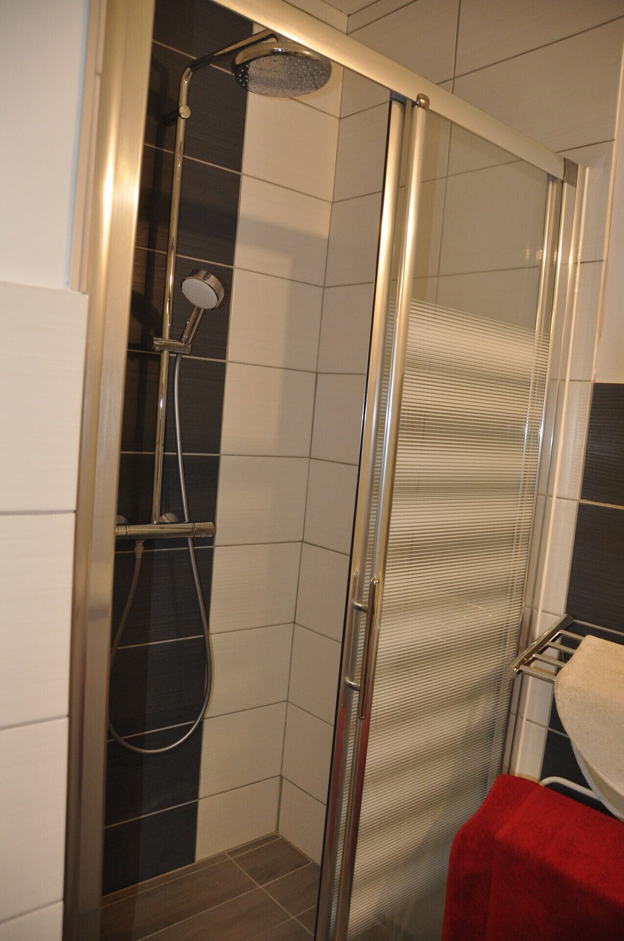 A shower with a glass door, a handheld showerhead, and a wall-mounted faucet.