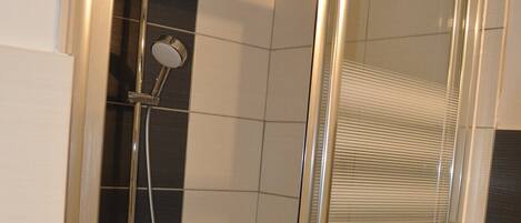 A shower with a glass door, a handheld showerhead, and a wall-mounted faucet.