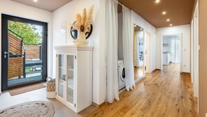A spacious hallway with a wooden floor, a white door, and a view of a garden outside. - Holiday flat ‘Bei Thérèse’ with balcony and Wi-Fi (Miltach)