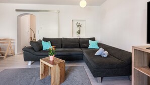 Ein modernes Wohnzimmer mit einem dunkelgrauen Ecksofa, einem Holztisch und einem grauen Teppich.