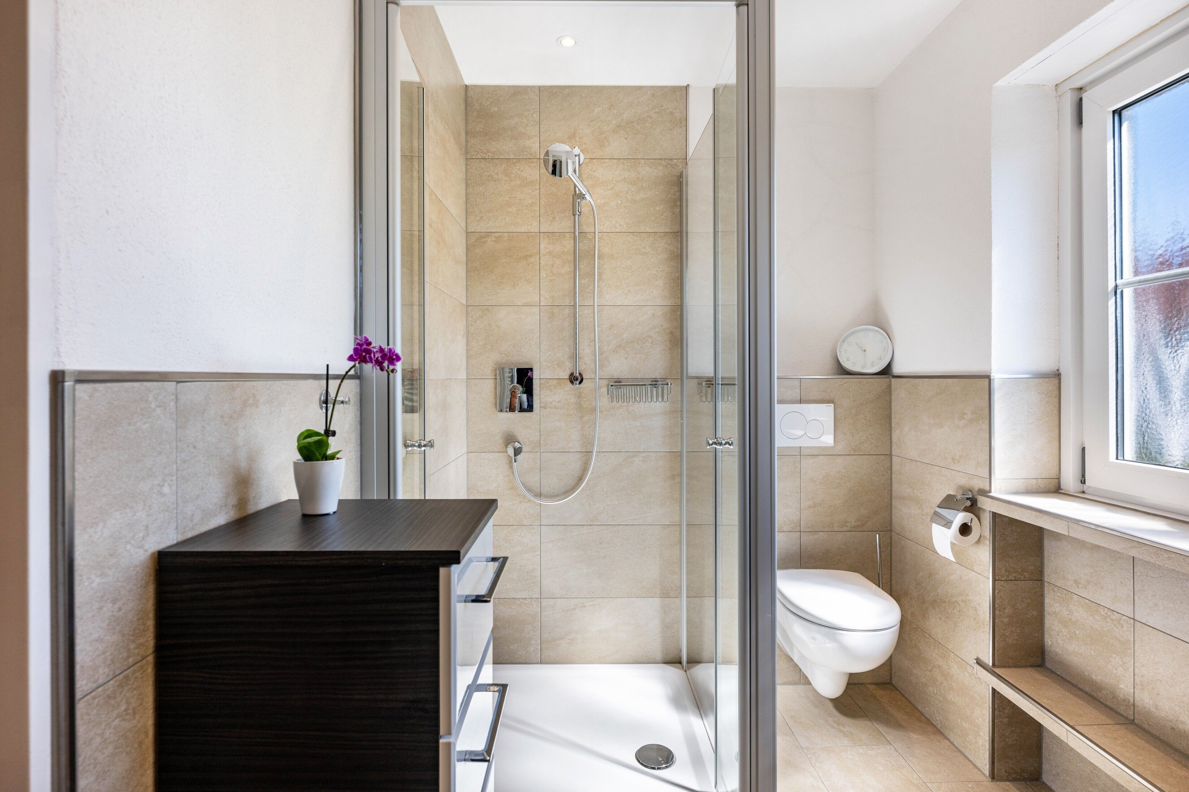 Ein modernes Badezimmer mit einer Duschkabine aus Glas, einer weißen Toilette und einem dunklen Holzwaschtisch.