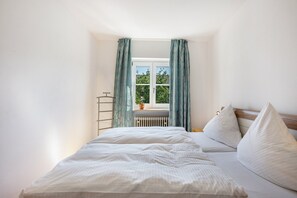 A bedroom with a bed, a radiator, and a window with curtains. - Charming Holiday Home with Private Garden by Lake Chiemsee (Prien am Chiemsee)