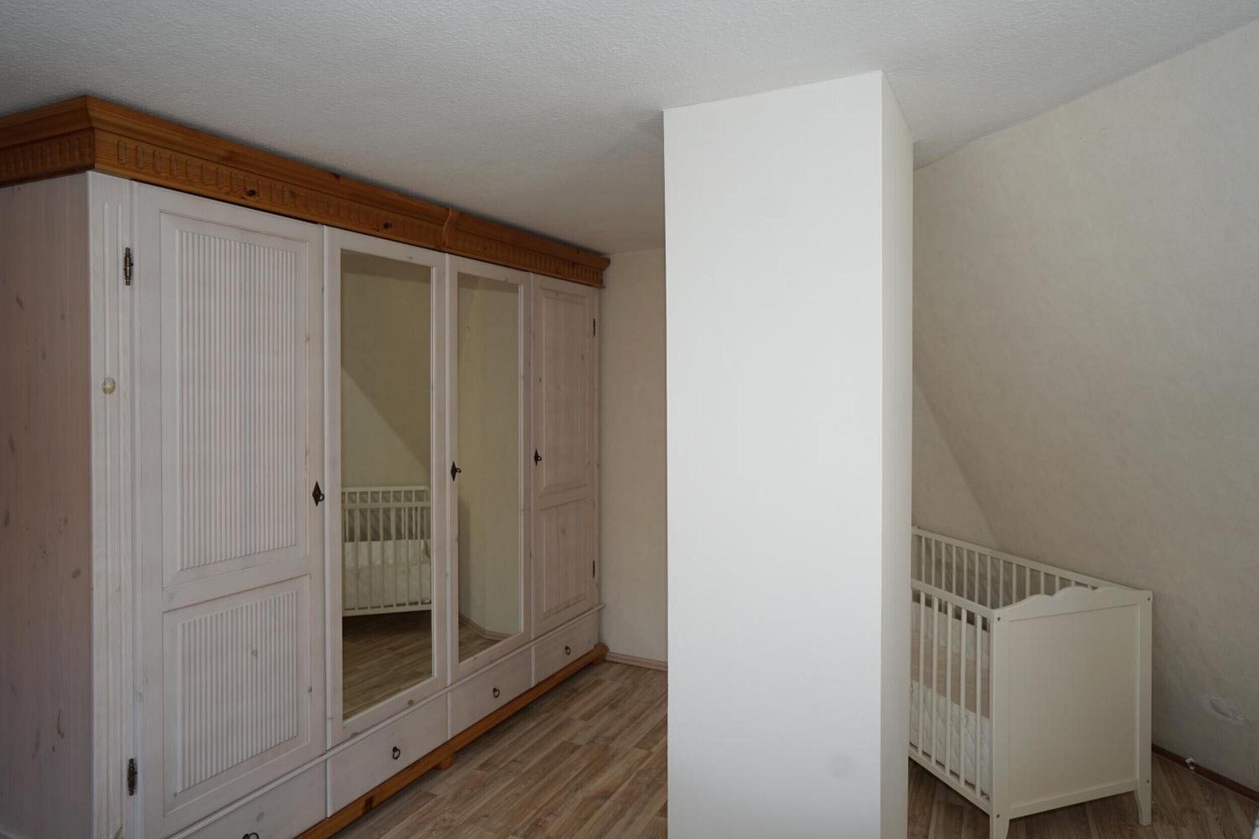 A room with a large white wardrobe, a white crib, and a wooden ceiling.