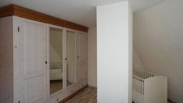 A room with a large white wardrobe, a white crib, and a wooden ceiling.