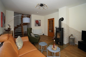 A living room with a sofa, a chair, a table with bottles, a fireplace, a staircase, and a door.