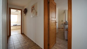 Un couloir avec une porte en bois, un tableau représentant un vélo accroché au mur et une fenêtre donnant sur un paysage.