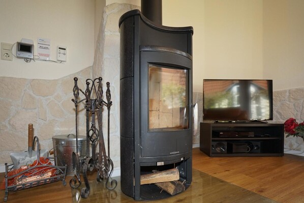 A wood-burning stove with a TV, a stone wall, and a fireplace tool rack.