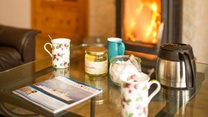 Une pièce chaleureuse avec une cheminée, une table en verre sur laquelle repose un magazine et une machine à café.
