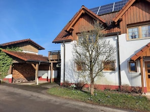 A two-story house with a sloped roof, solar panels, and a small tree in the front yard.
