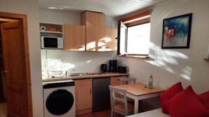 A compact room with a bed, a small table, a washing machine, a sink, and a window.