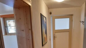 A hallway with wooden flooring, a door, a painting on the wall, and a bench.