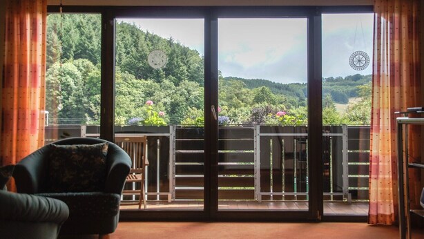 A room with a large sliding glass door leading to a balcony with a view of a forested hillside. - Holiday Apartment "Rauber Marie Theres" with Private Garden, Balcony & Wi-Fi (Abentheuer)