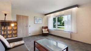A modern living room with a glass coffee table, a sofa, a chair, and a fireplace. - Apartment 'Bubach' with Private Terrace, Shared Garden and Wi-Fi (Bubach)