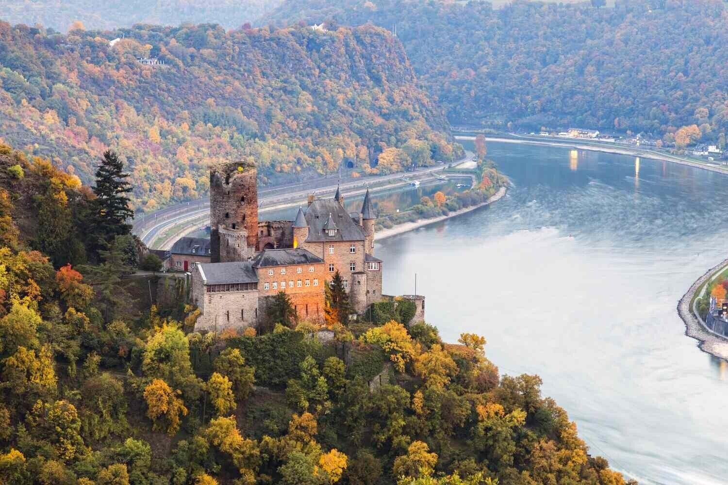 Eine Burg, im Hintergrund ein Fluss, umgeben von Herbstlaub.