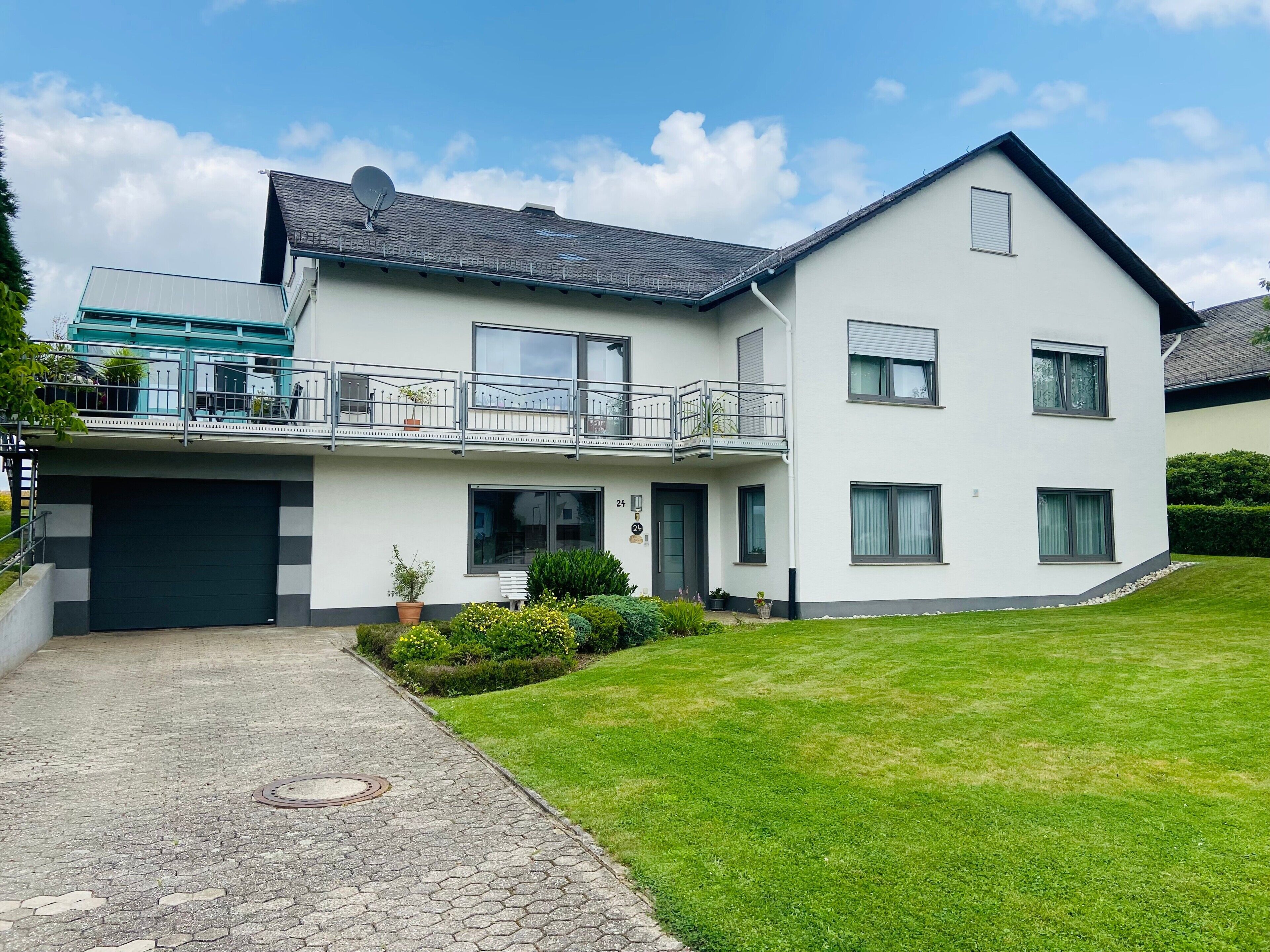 A two-story residential building with a garage, a balcony, and a well-maintained lawn.