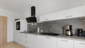 A modern kitchen with white cabinets, a black range hood, a stainless steel sink, and a coffee maker. - Apartment 'Bubach' with Private Terrace, Shared Garden and Wi-Fi (Bubach)