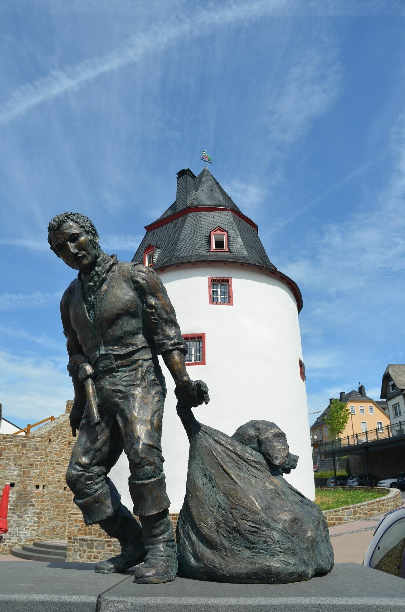 A statue of a man with a dog in front of a white building with a red roof.