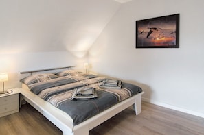 A neatly made bed with striped bedding, a bedside table with a lamp, and a framed picture on the wall. - Apartment 'Swaalvkenüst' with Balcony and Wi-Fi (Moormerland)