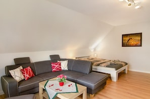 A modern living room with a sectional sofa, a small table with a vase, and a painting on the wall. - Apartment 'Swaalvkenüst' with Balcony and Wi-Fi (Moormerland)