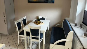Un coin repas avec une table et des chaises blanches, un tableau au mur et un meuble sur le côté gauche.