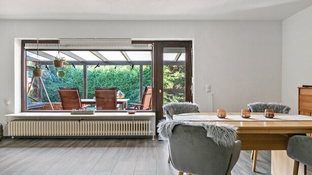 Un espace repas comprenant une table et des chaises, avec vue sur la verdure à l’extérieur, et une fenêtre donnant sur un patio.