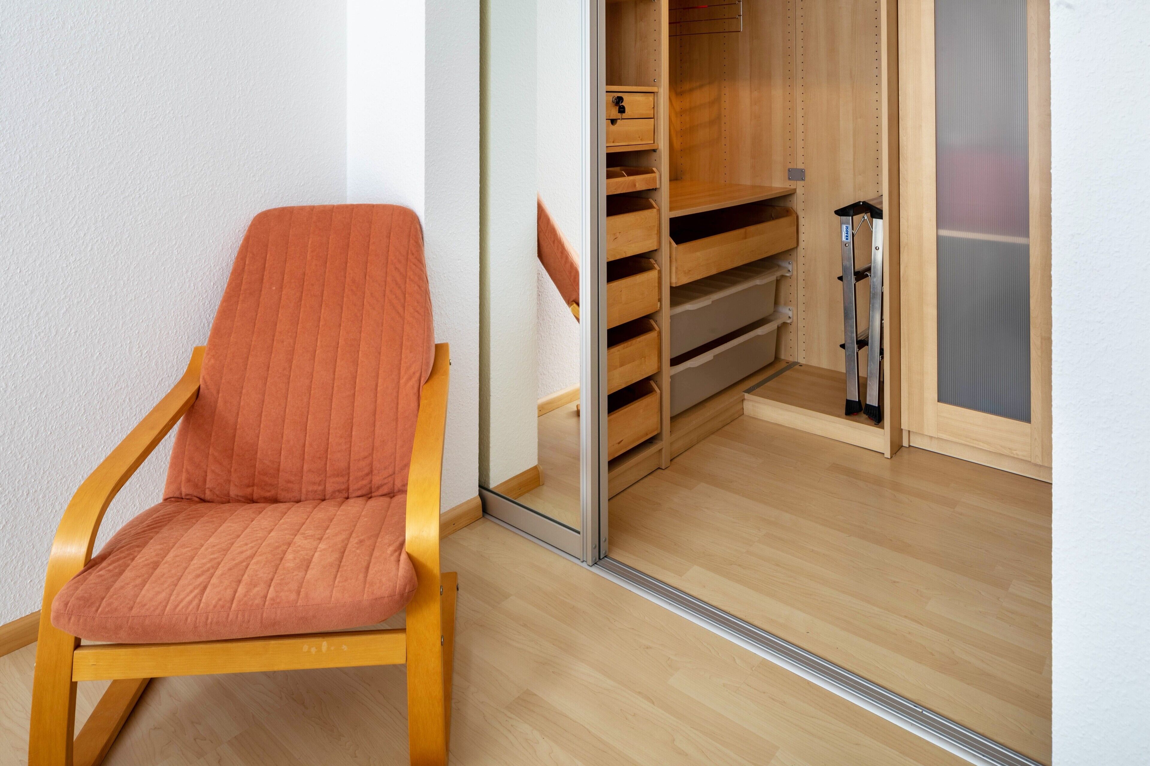 A wooden chair with a cushion, a wooden closet with shelves, and a sliding door.