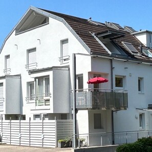 A two-story building with a balcony, a red umbrella, and a white exterior.