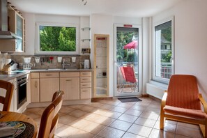 A kitchen with a dining area, a red umbrella outside, and a view of greenery.