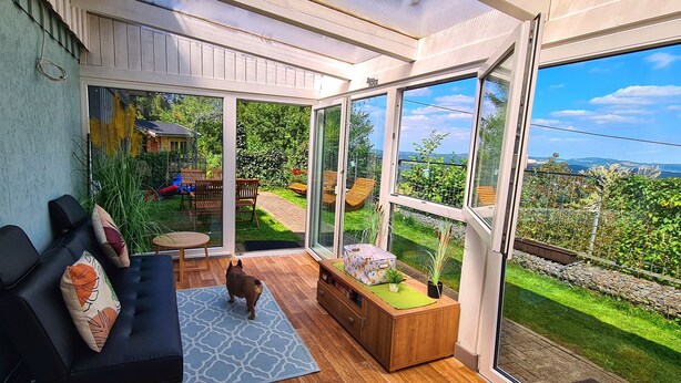 Una habitación moderna con un amplio ventanal corredera que da a un jardín, un sofá, una mesita y un mueble con una planta.