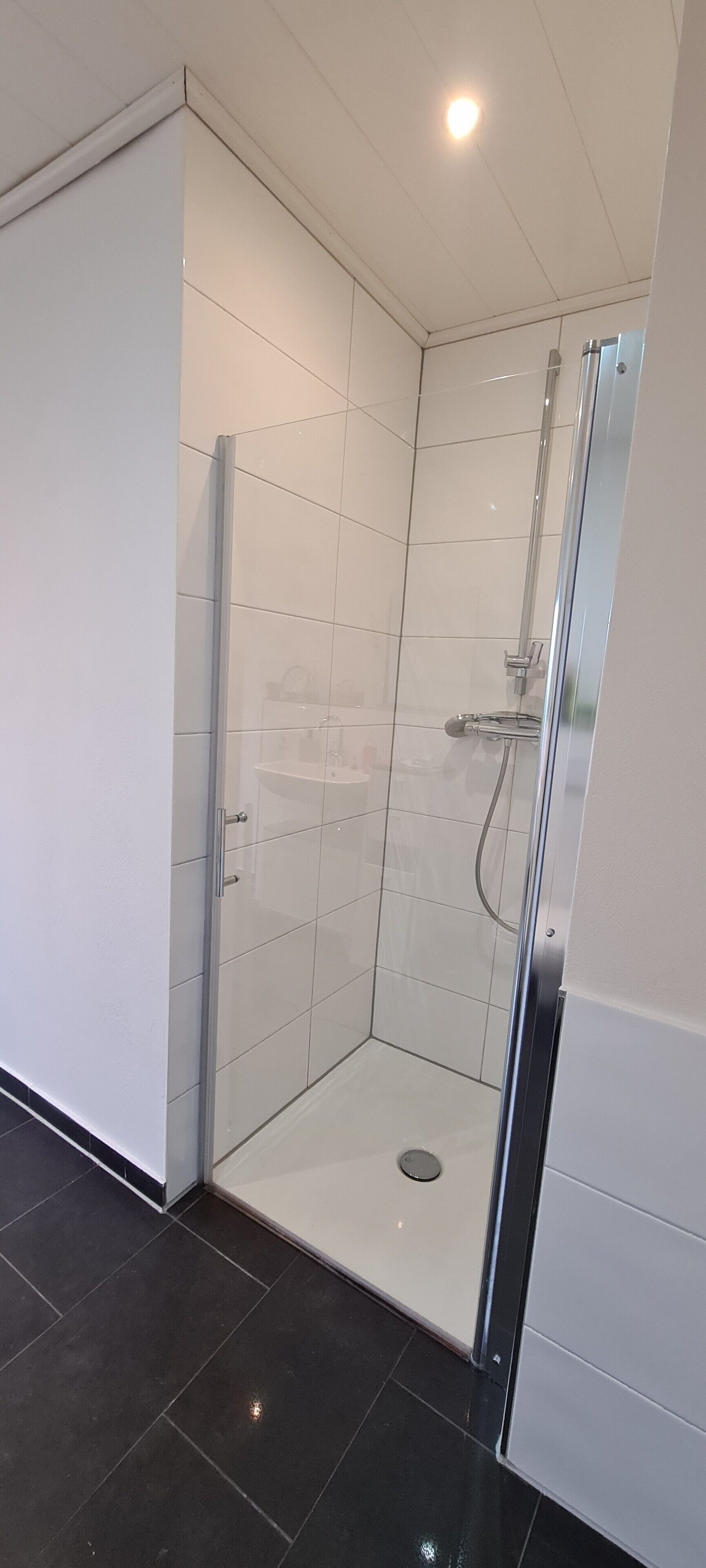 Un bagno moderno con box doccia in vetro, pareti piastrellate di bianco e pavimento nero.