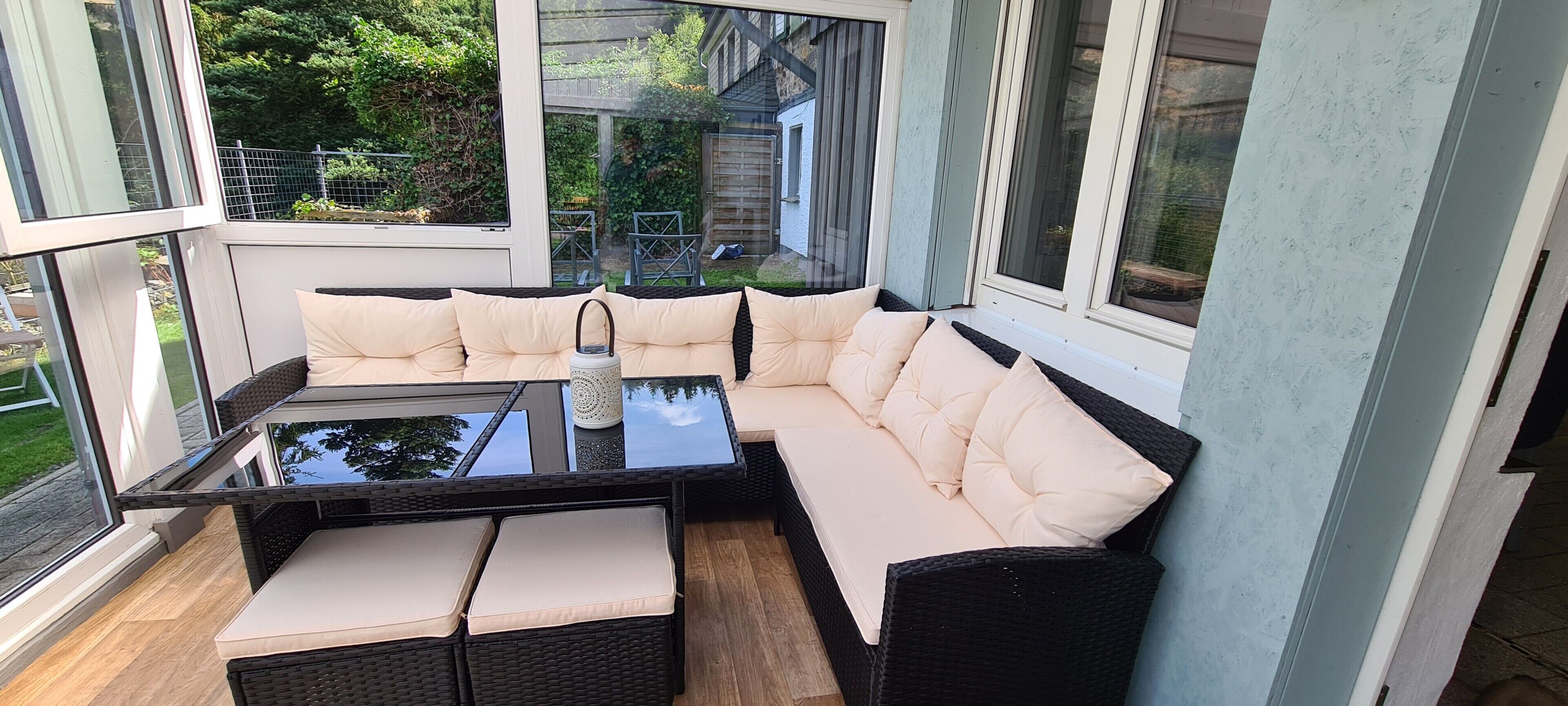 Une véranda avec une table en verre, des sièges confortables et une vue sur le jardin arrière.