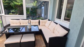 Une véranda avec une table en verre, des sièges confortables et une vue sur le jardin arrière.