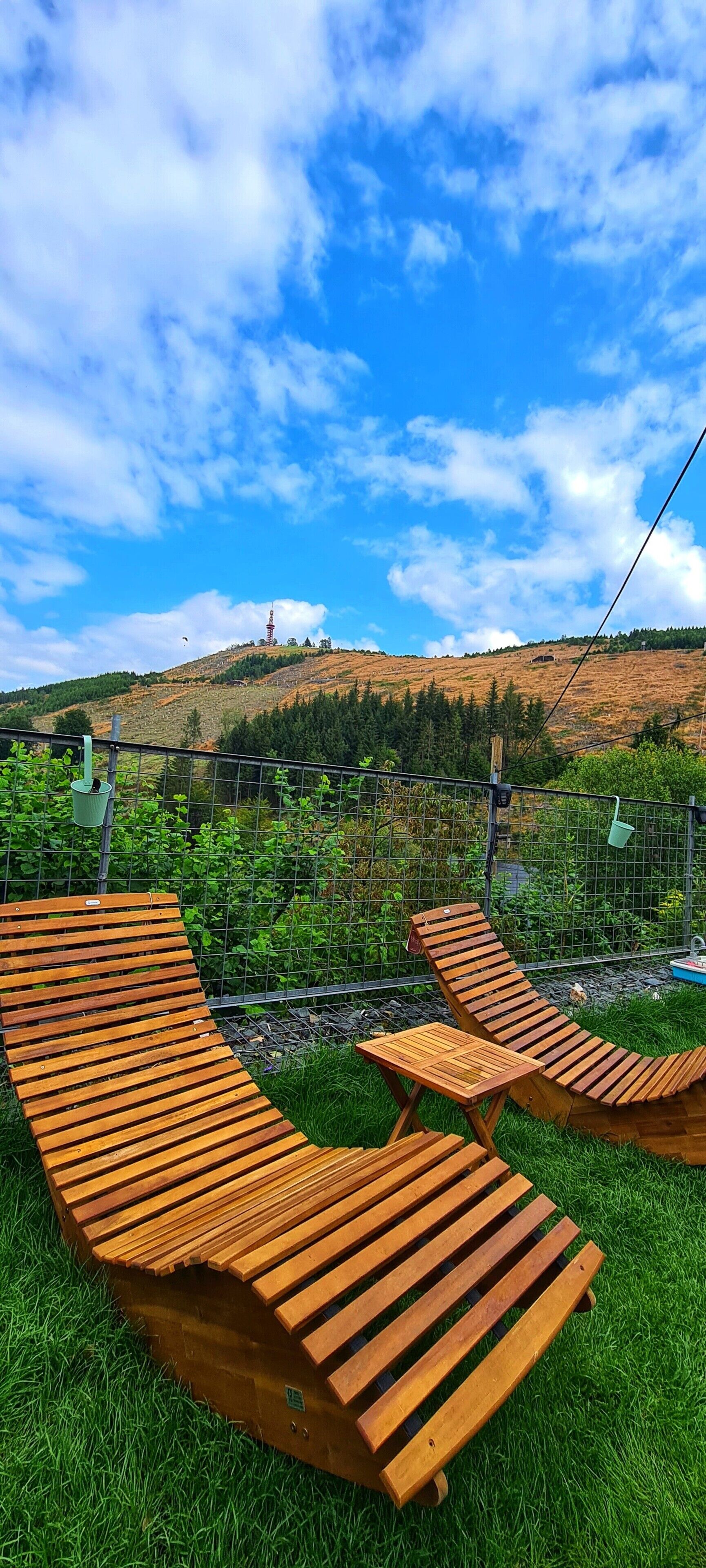 Eine Holzterrasse mit Liegestühlen, ein Metallzaun und ein Hügel mit einem Turm im Hintergrund.